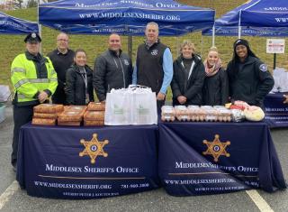 MSO staff outside behind two tables filled with Thanksgiving meal kit items including pies, turkeys and eggs.